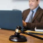 A focused lawyer working on a laptop with a gavel on the desk, indicating legal proceedings.