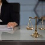 Balance scales on a desk in a professional office with a blurred businesswoman in the background.